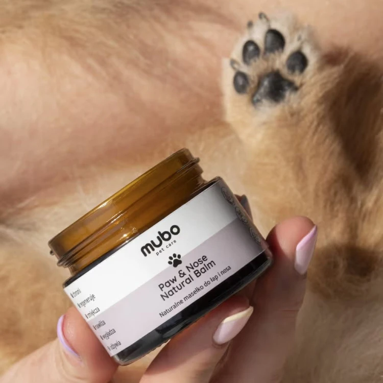 Balsam Mubo Paw &amp; Nose Natural Balm trzymany w dłoni obok psiej łapy