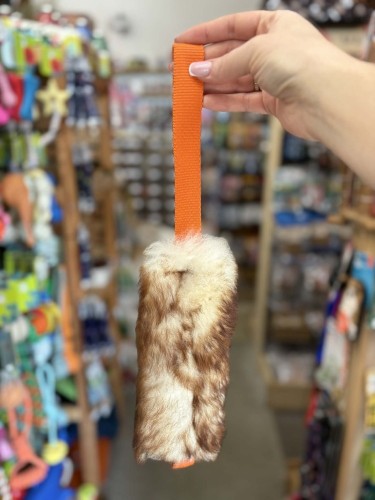 Szarpak dla psa Psarvard Tika z futra owczego i pomarańczową taśmą trzymany w dłoni