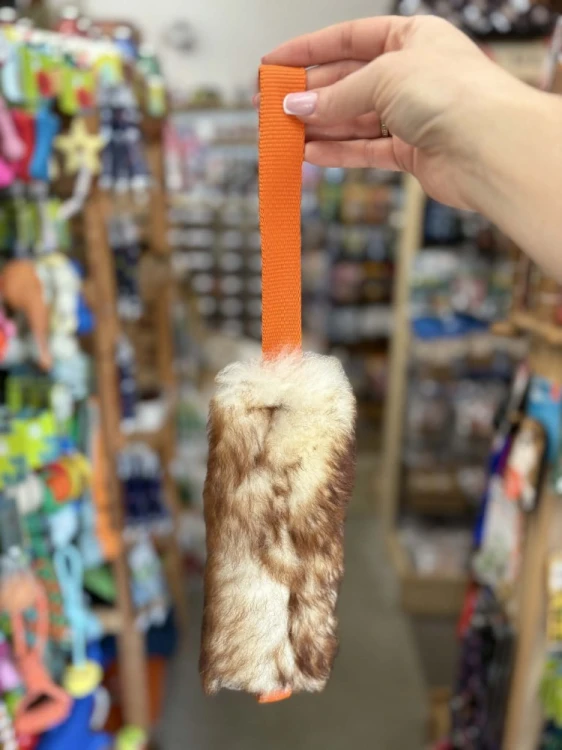 Szarpak dla psa Psarvard Tika z futra owczego i pomarańczową taśmą trzymany w dłoni